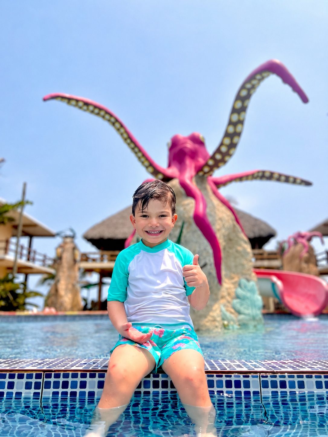 Niño sentado en la orilla de la piscina frente al tobogán con forma de pulpo.