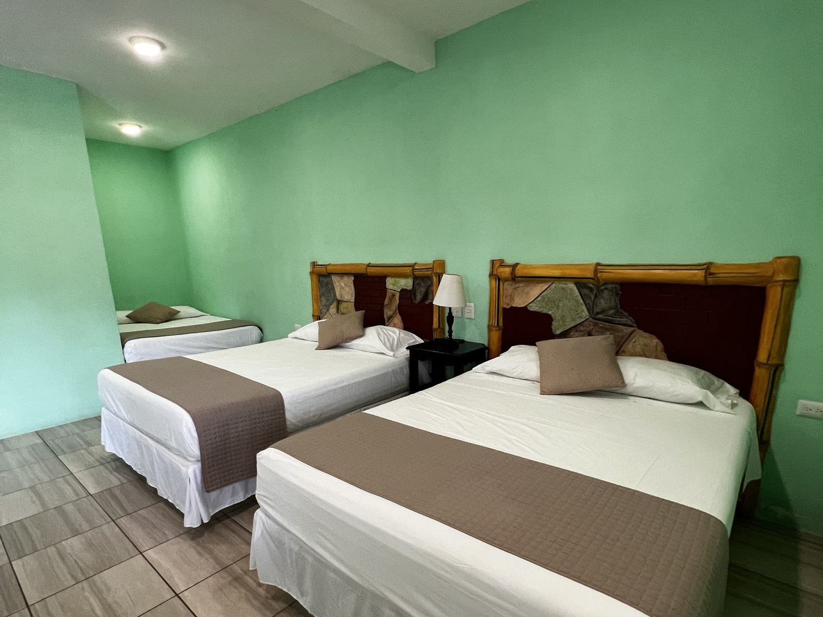 Habitación del hotel con tres camas, cabeceras de madera y ropa de cama blanca.