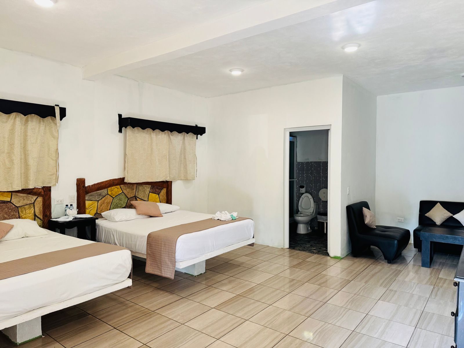 Vista amplia de una habitación con camas, zona de estar y entrada al baño.